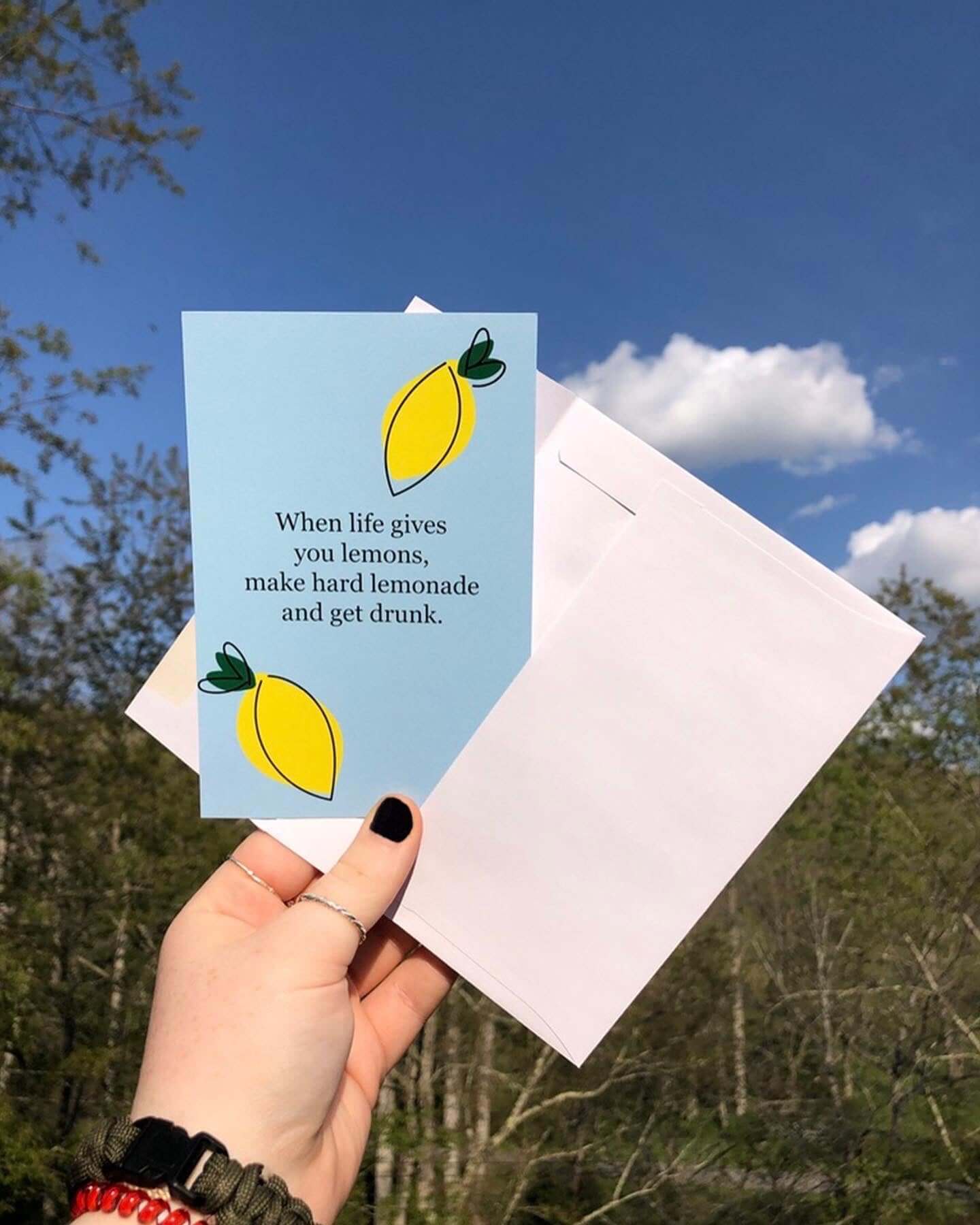 Hand holding Hard Lemonade postcard and envelope outside