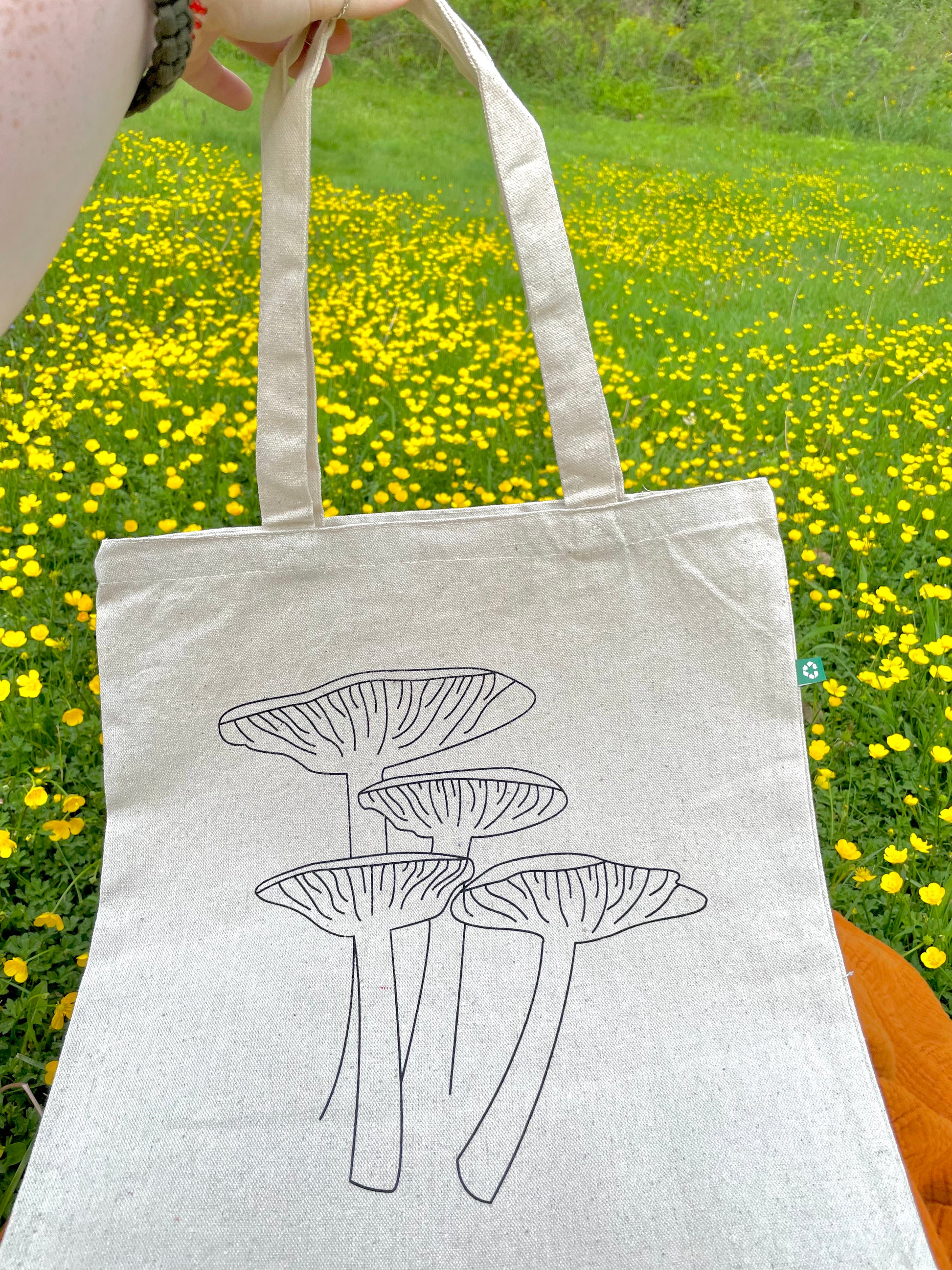 Holding Keep it Shroomy tote up in front of flowers