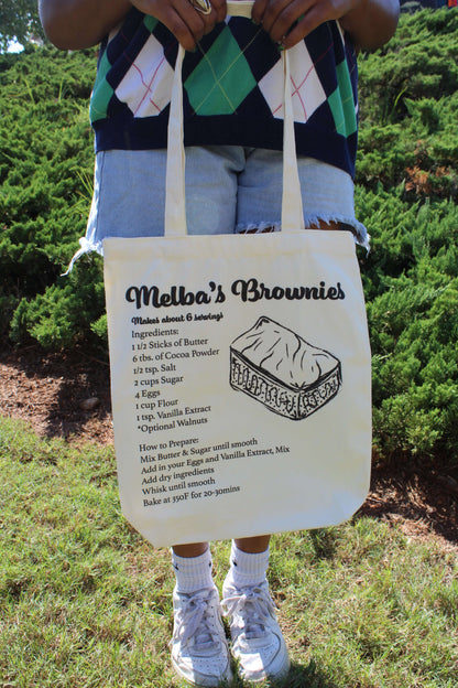 Girl holding Melba's Brownies tote in front of body with two hands