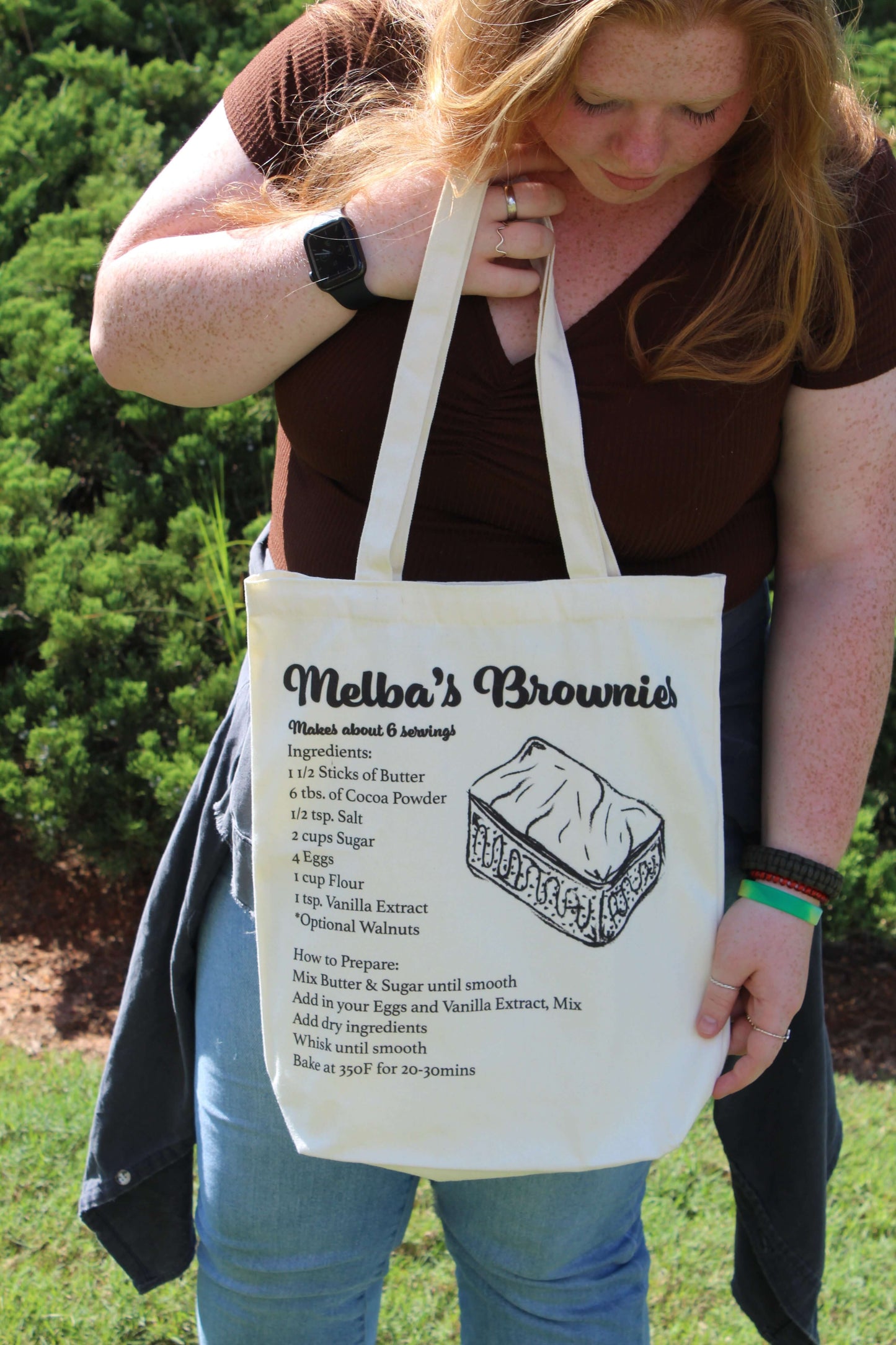 Girl holding up Melba's Brownies tote looking down