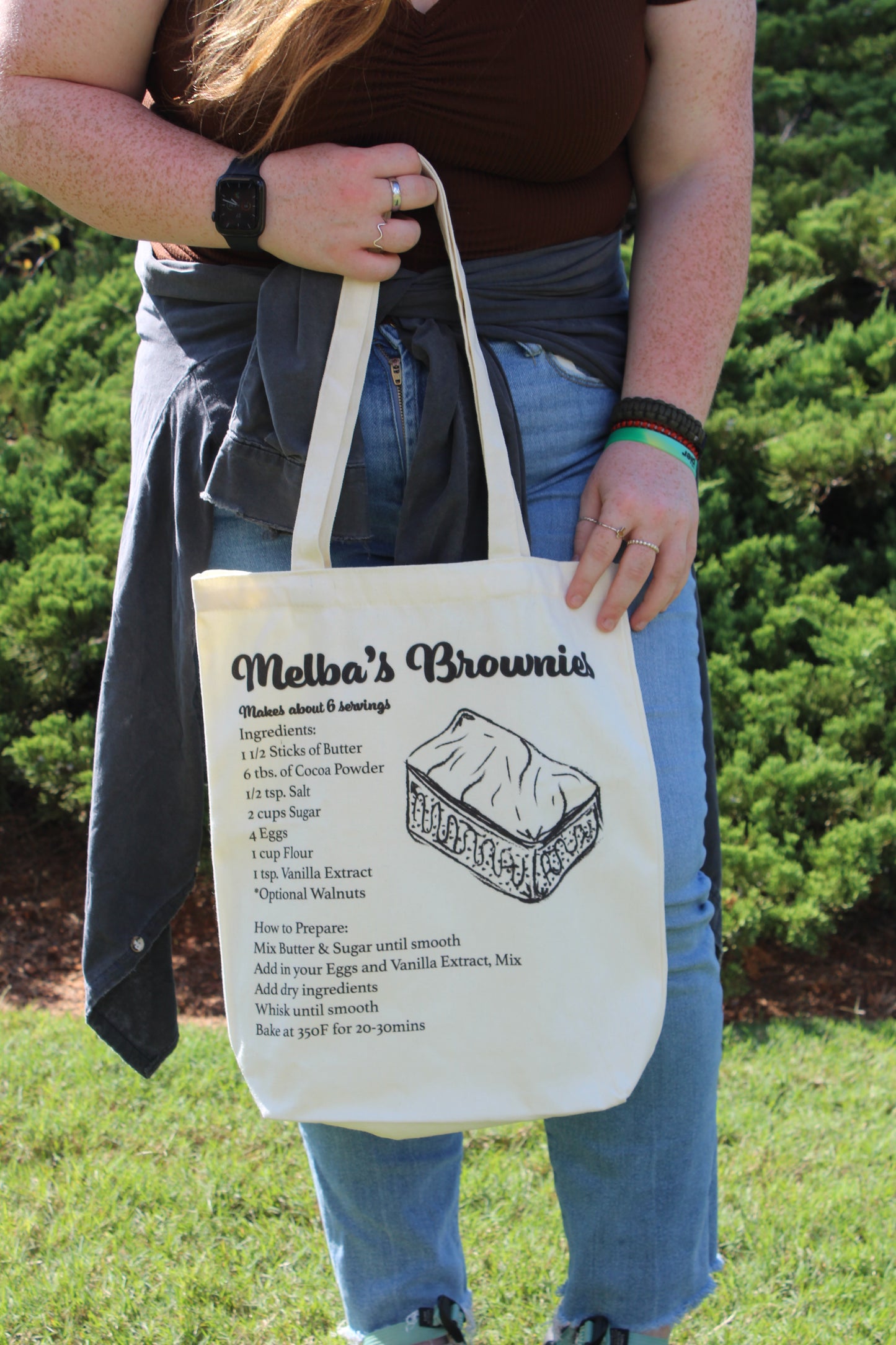 Girl holding Melba's Brownies tote outside in front of body