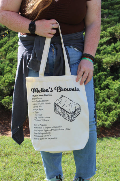 Girl holding Melba's Brownies tote outside in front of body