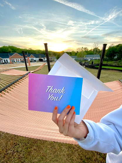 Hand holding blue and pink thank you card with envelope in sunset