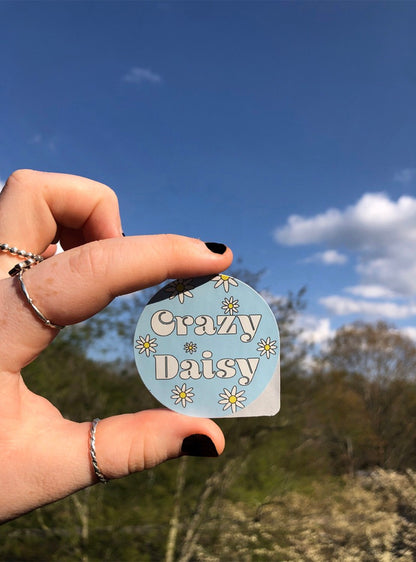 Girl holding Crazy Daisy sticker outside with two fingers