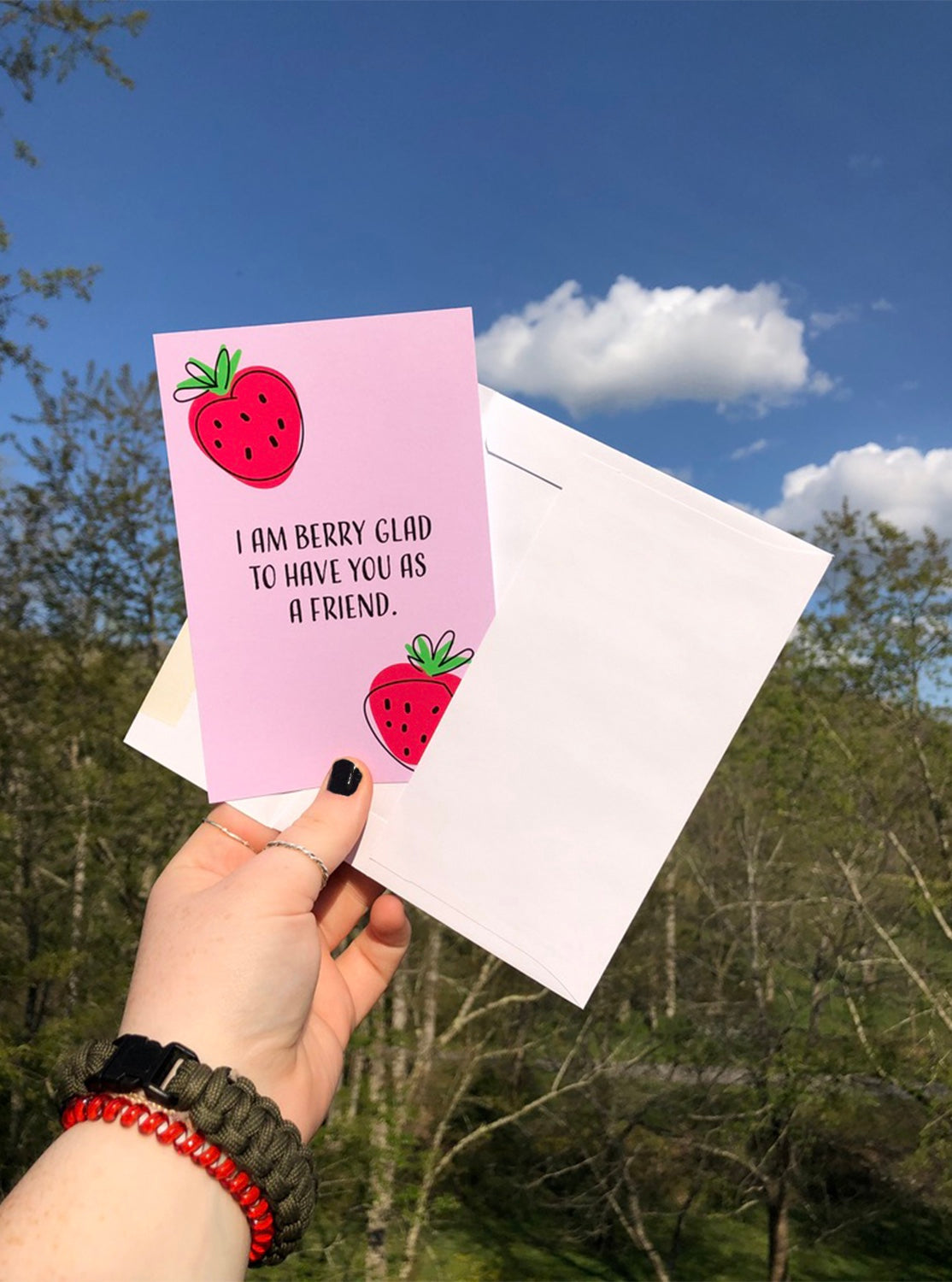 Hand holding Very Berry postcard and envelope outside