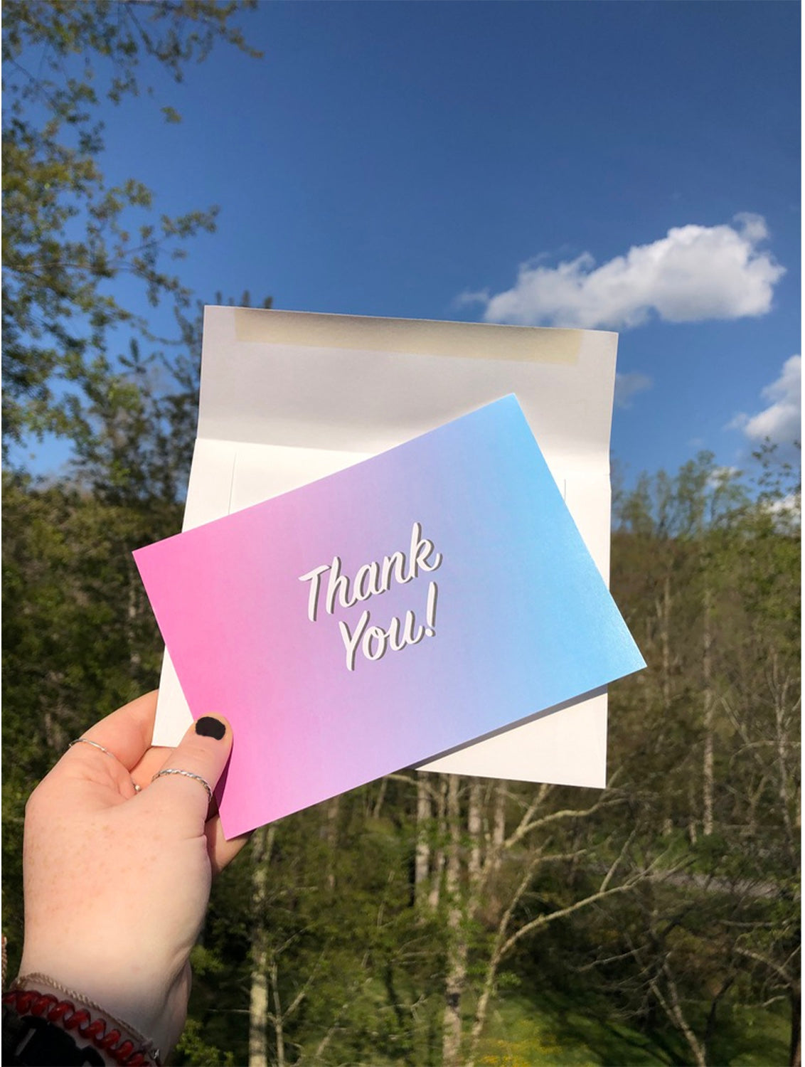 hand holding blue and pink thank you card with envelope outside